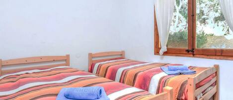 A room with two wooden beds, each with a striped bedspread and a blue towel.