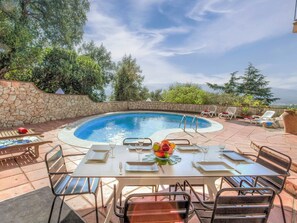 A poolside area with a table set for dining, surrounded by lounge chairs and a stone wall. - Stunning private villa for 6 people with private pool, A/C, WIFI, TV and panoramic view (Les Teules)