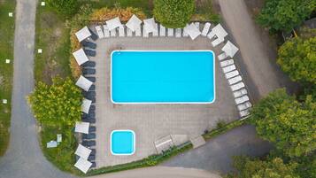 An aerial view of a swimming pool area with a rectangular pool, lounge chairs, and a smaller pool.