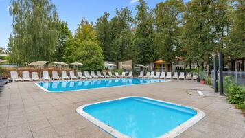 A rectangular swimming pool with a tiled deck, surrounded by white lounge chairs and umbrellas.