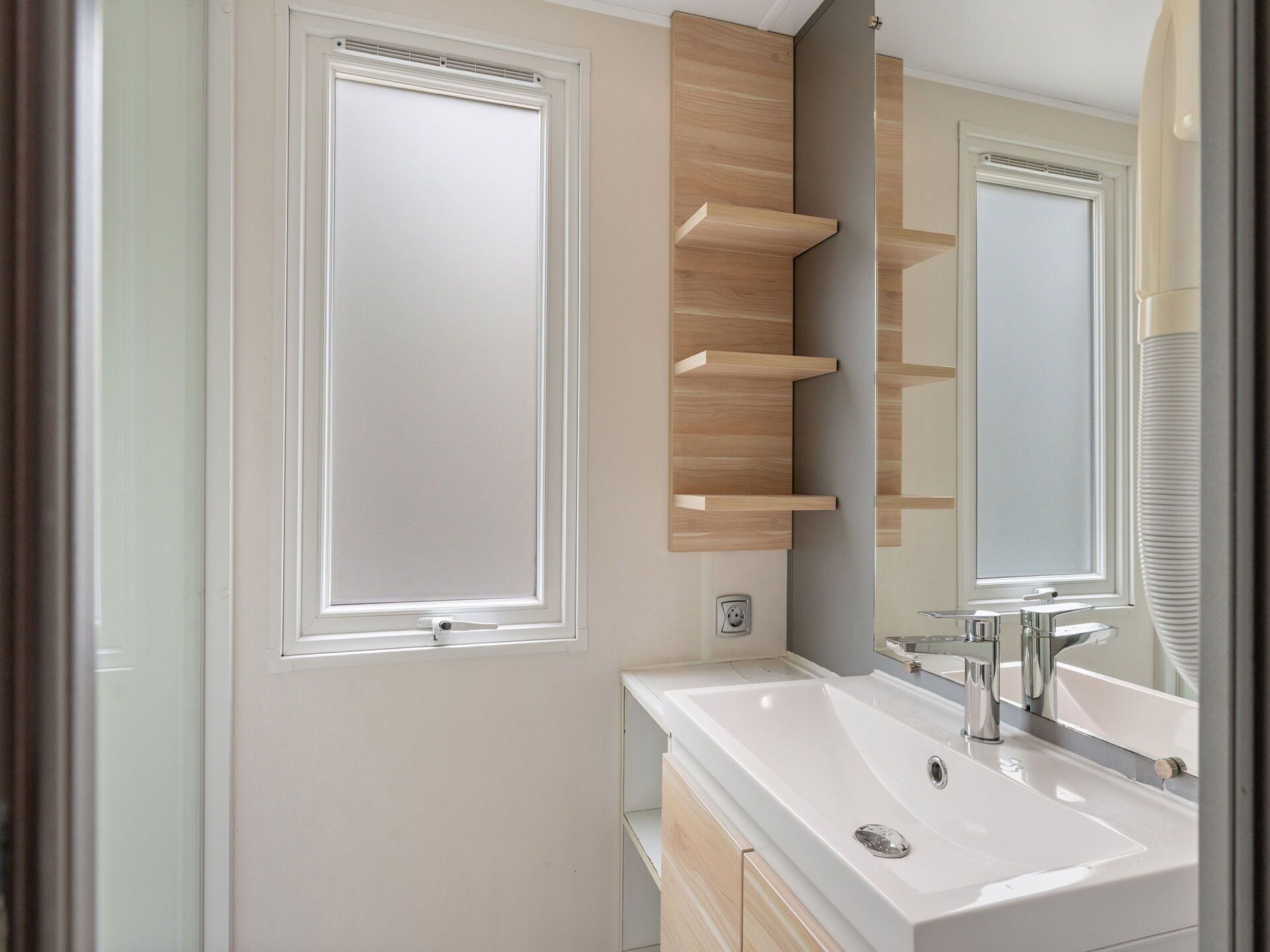 Un bagno con un lavandino bianco, uno specchio e mensole in legno.