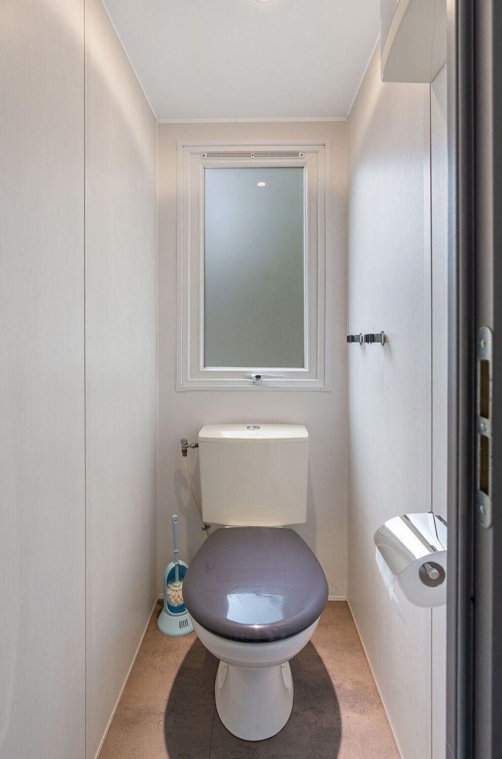 Et lille, aflangt badeværelse med toilet, et vindue og en håndtørrer.