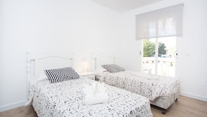 Ein Schlafzimmer mit zwei Betten, weißen Wänden, einem großen Fenster und einer Deckenleuchte.
