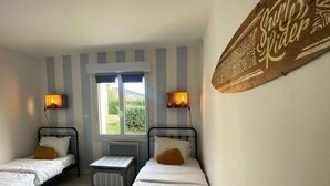 A room with two single beds, a small table, and a window with curtains. - A 2 bedroom gite sleeping 4 plus a cot with access to a heated covered pool. (Henansal)