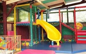 Ein Spielbereich für Kinder mit einer gelben Rutsche, Klettergerüsten mit Netzen und einem Ballbecken.