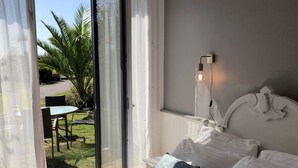A bedroom with a bed, pillows, and a nightstand. There is a window with curtains, a view of a garden outside. - A 2 bedroom gite sleeping 4 plus a cot with access to a heated covered pool. (Henansal)