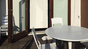A patio area with a round table and chairs, a white chair, a wooden door, and a tiled roof.
