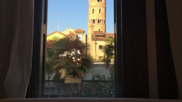 A view of a tall tower with a pointed roof through a window with curtains.