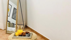 A corner of a room with a wicker ottoman, a tray with breakfast items, and a glass of orange juice.