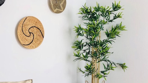 A room with a woven plant pot on a tiled floor, a woven wall hanging, and a patterned pillow on a dark sofa.