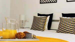 A neatly made bed with a yellow blanket, a breakfast tray with orange juice, a croissant, and a patterned mug.