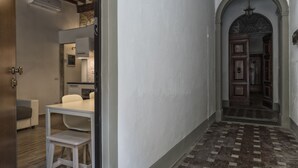 A hallway with a tiled floor, a white wall, and an arched doorway leading to a room with a wooden door. - GUELFA HOUSE: restructuring, on the ground floor, comfortably accommodates 6 people  (Firenze)