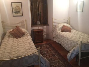 Una habitación con dos camas individuales, una mesita de noche de madera, una ventana con contraventanas de madera y un cuadro en la pared.