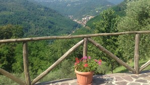 Terraza empedrada con barandilla de madera que da a un valle con un pueblo en la distancia.