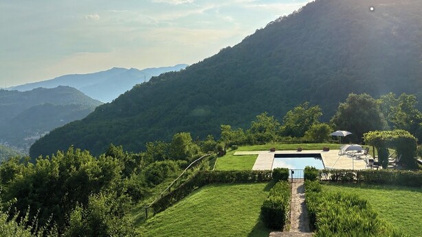 Un área de piscina con un sendero de piedra, rodeada de exuberante vegetación y colinas al fondo.