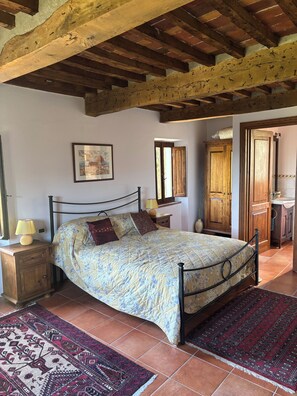 Un dormitorio con cama, cabecera de madera, mesitas de noche, una alfombra y un cuadro en la pared.