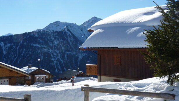 Een houten chalet met een met sneeuw bedekte dak, een houten hek en een berg op de achtergrond.