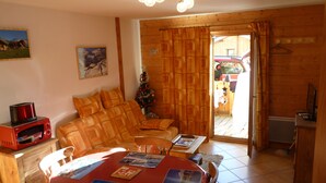 Een gezellige woonkamer met een houten bank, een eettafel met foto’s, een rode magnetron en een kleine kerstboom.