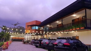 A hotel with a modern design, featuring a multi-story structure, a covered outdoor area, and a parking lot with several vehicles. - Borobudur Bed & Breakfast - Hostel (Mungkid)