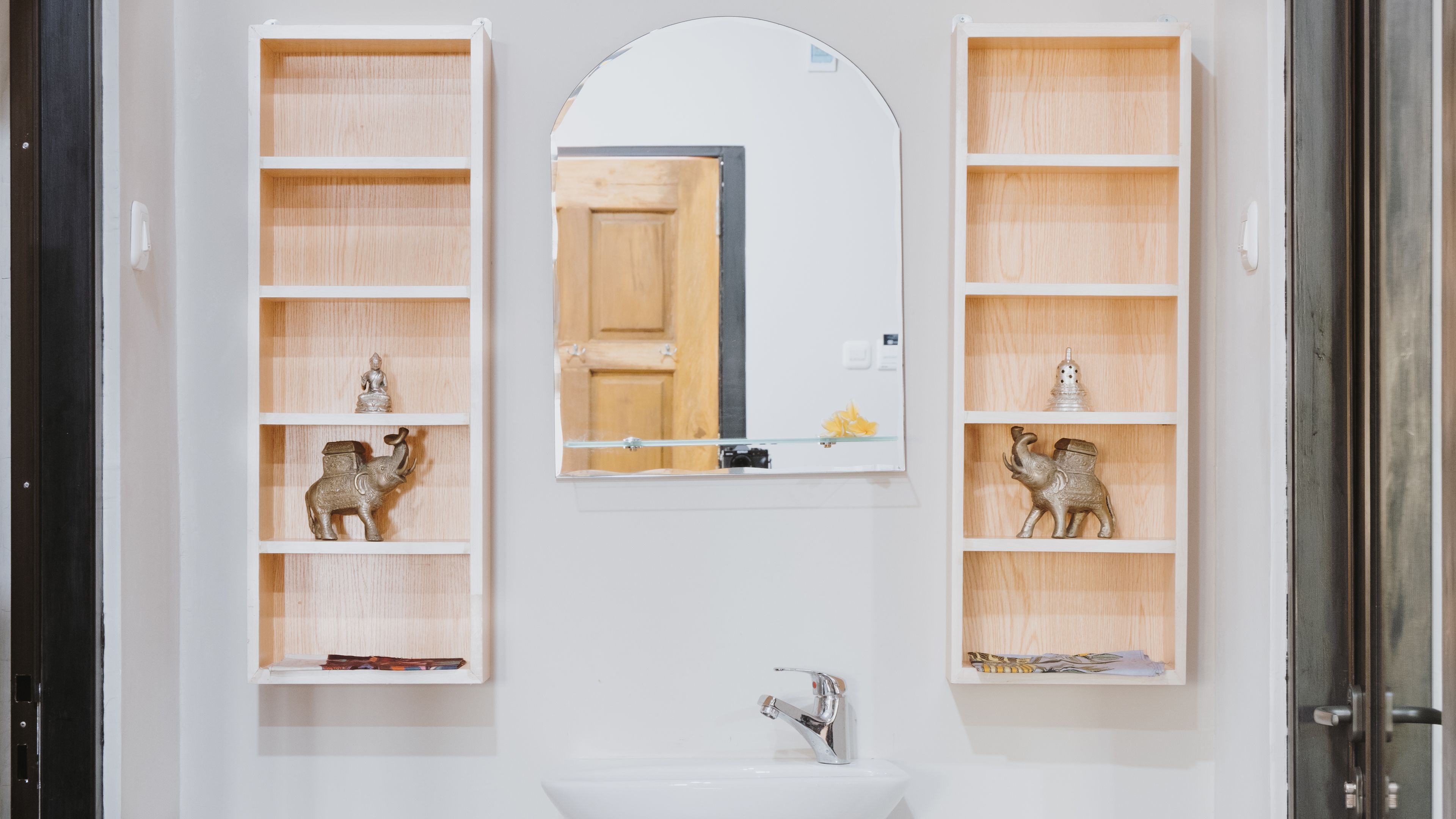 A bathroom with a white sink, a mirror, and two shelves with decorative items.