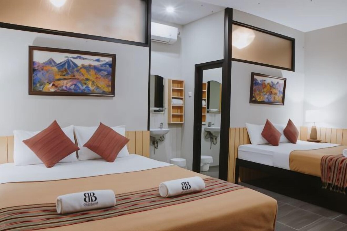 Une chambre d’hôtel avec deux lits, un grand tableau au mur, un miroir et une petite salle de bain.