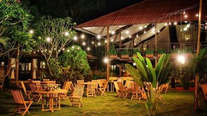 An outdoor dining area with wooden tables and chairs, string lights, and potted plants. - Borobudur Bed & Breakfast - Hostel (Mungkid)