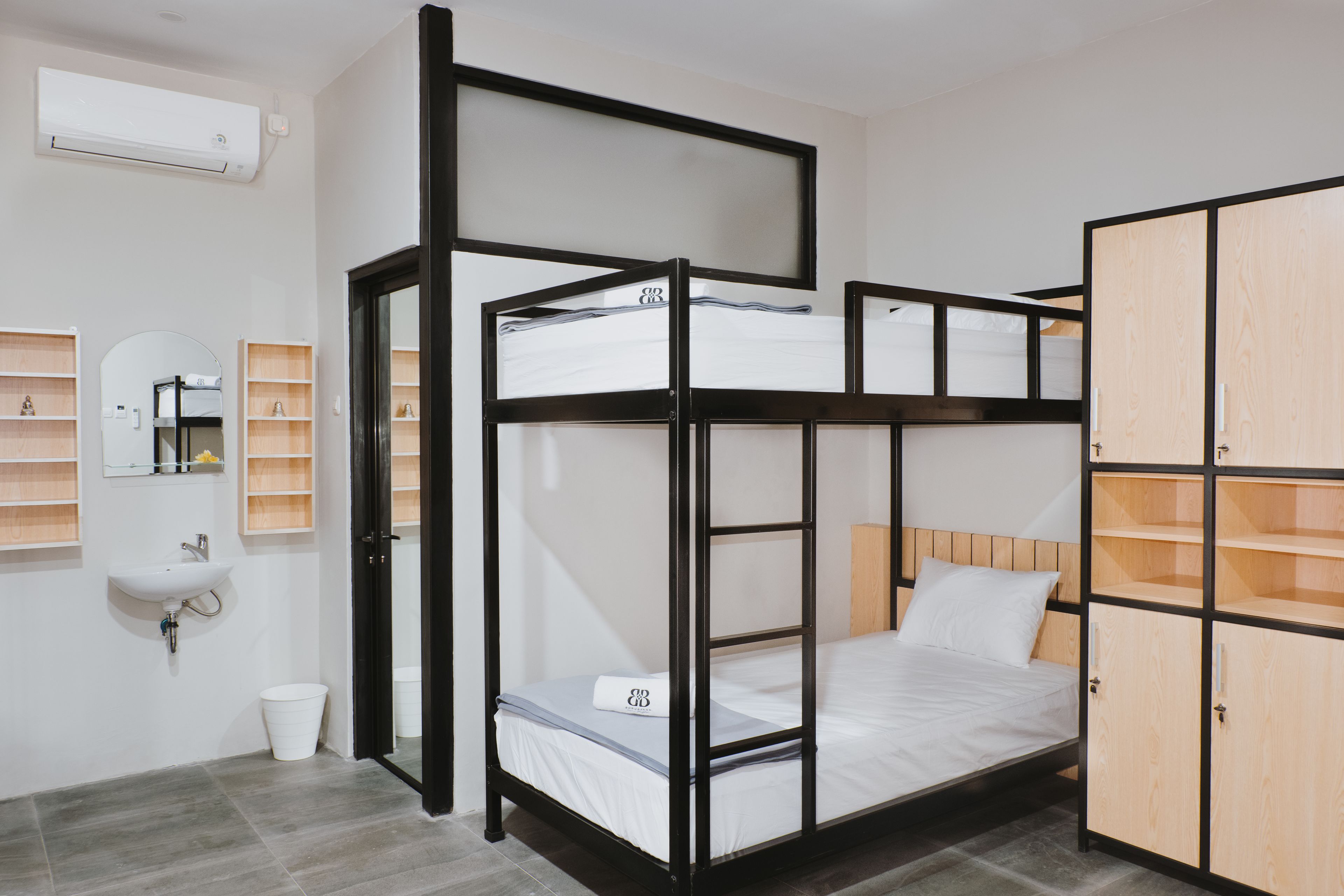 A bunk bed room with a wooden wardrobe, a sink, and a mirror.