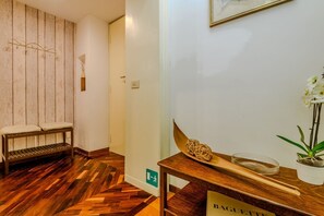 A wooden bench with a towel, a wooden table with a bowl and chopsticks, and a wall-mounted picture frame.