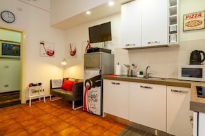 A compact kitchen with a microwave, sink, and a flat-screen TV mounted above the stove.