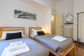 A hotel room with two beds, a painting of the Colosseum, a mirror, and a radiator.