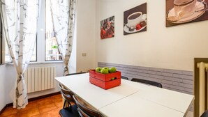 Zona pranzo con tavolo, sedie, termosifone e opere d'arte appese al muro.