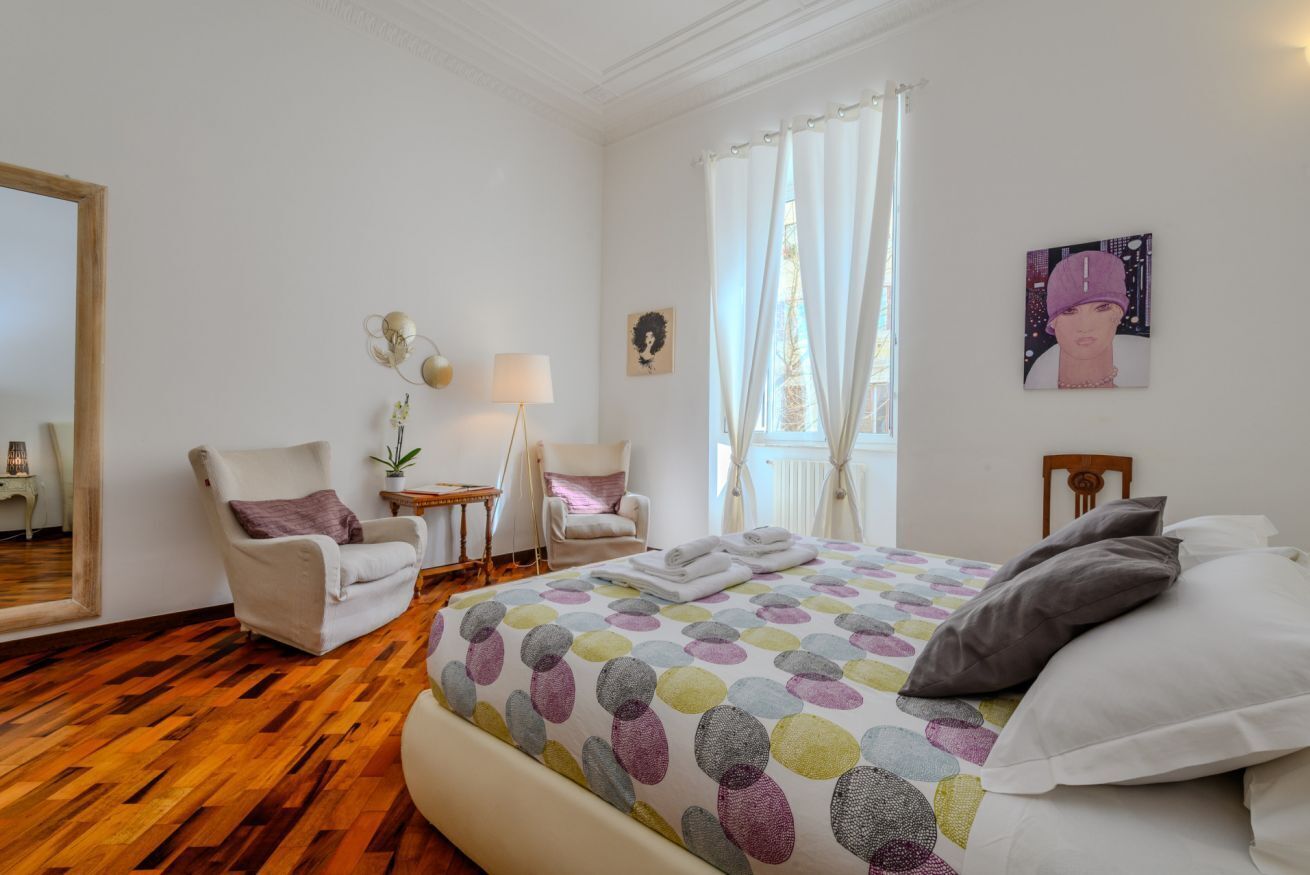 A bedroom with a large bed, two chairs, a small table, and a mirror.