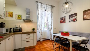 Una cocina compacta con armarios blancos, microondas, hervidor y zona de comedor con mesa y sillas.