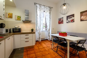 A compact kitchen with white cabinets, a microwave, a kettle, and a dining area with a table and chairs.