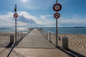 Uma passarela costeira com guarda-corpo, lixeiras e placas de indicação.