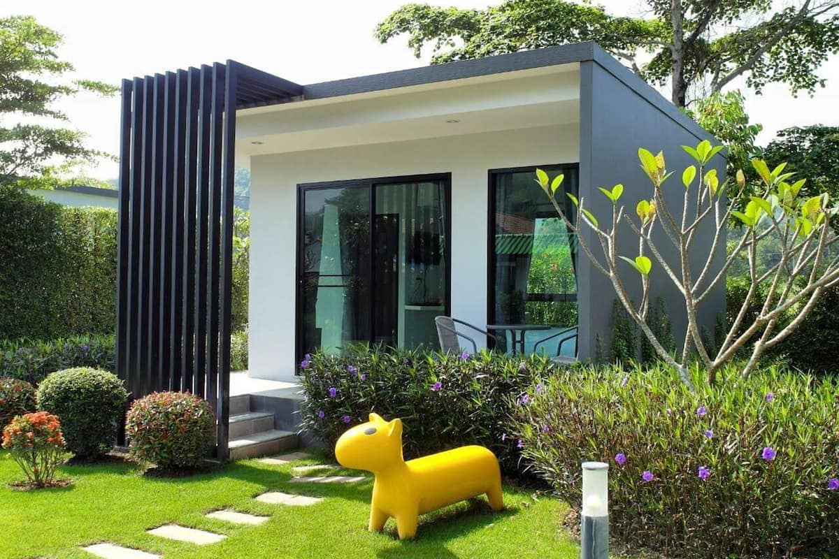 A modern house with a flat roof, large windows, and a well-maintained garden with a yellow sculpture.