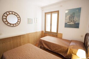 Une chambre avec deux lits, une fenêtre, un miroir et un tableau encadré au mur.
