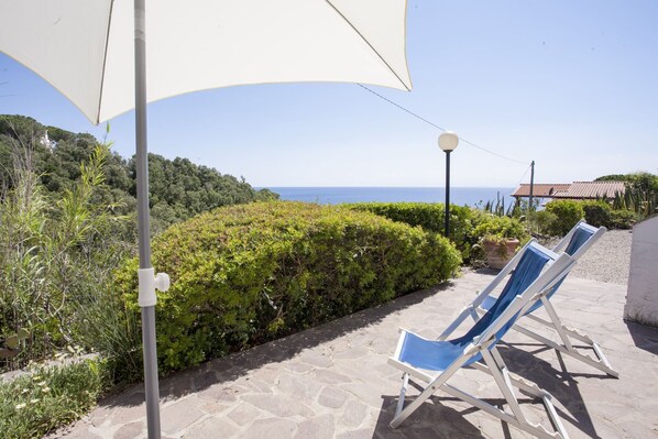 Un patio con dos sillones azules, una sombrilla blanca y vista al mar.