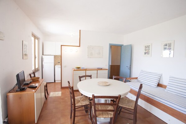 A compact living space with a kitchenette, a dining area with a round table and chairs, a sofa, and a bed.