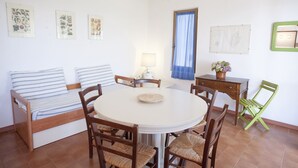 Een gezellige kamer met een bed, een ronde eettafel en stoelen. Er hangen kunstwerken aan de muur en er is een raam met gordijnen.