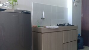 A kitchen with a Panasonic refrigerator, a gas stove, and a sink. - AGV Apartment Yogyakarta (Depok)