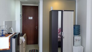 A compact hotel room with a kitchenette, a water dispenser, a wardrobe, and a door leading to a bedroom. - AGV Apartment Yogyakarta (Depok)