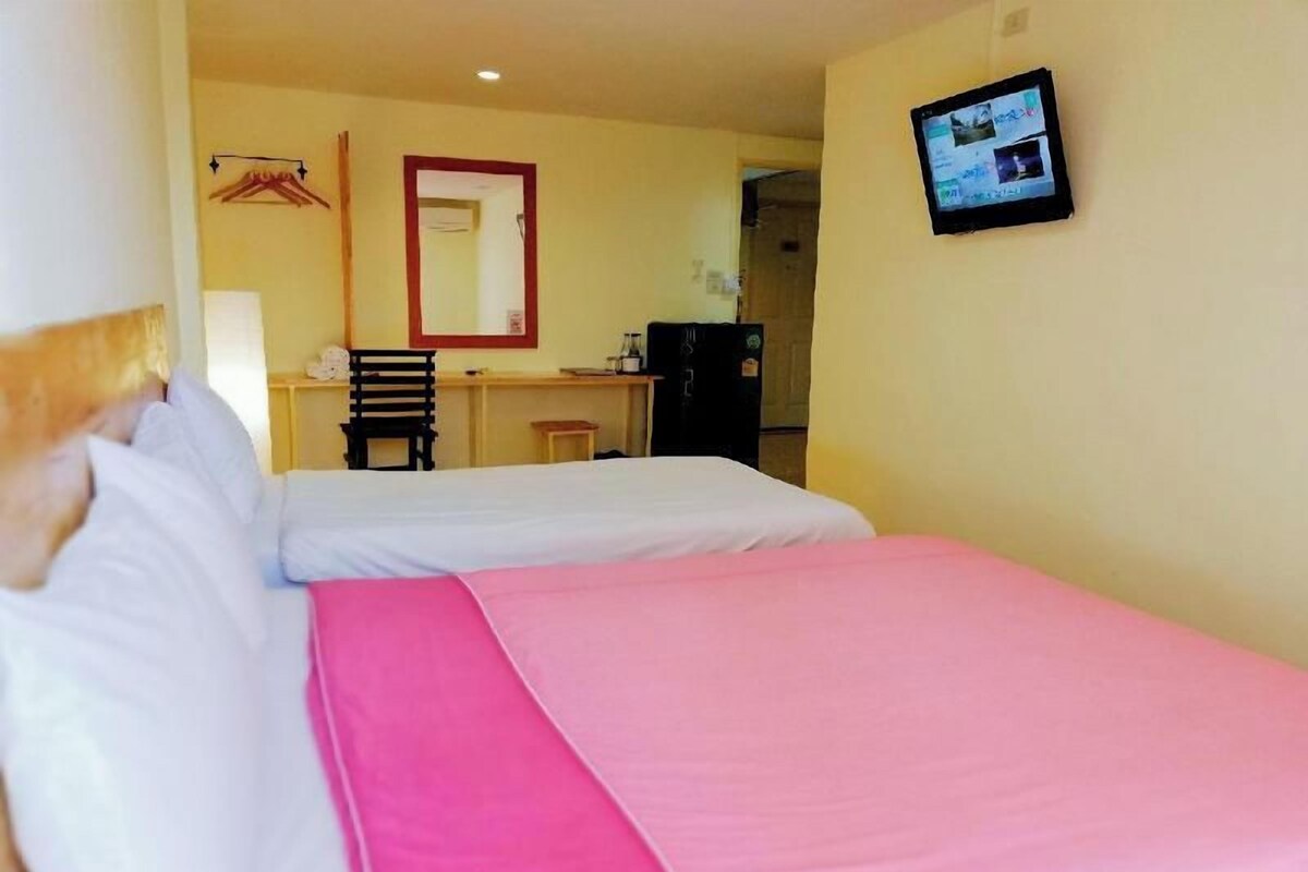 A hotel room with two beds, a desk, a chair, a mirror, and a television.