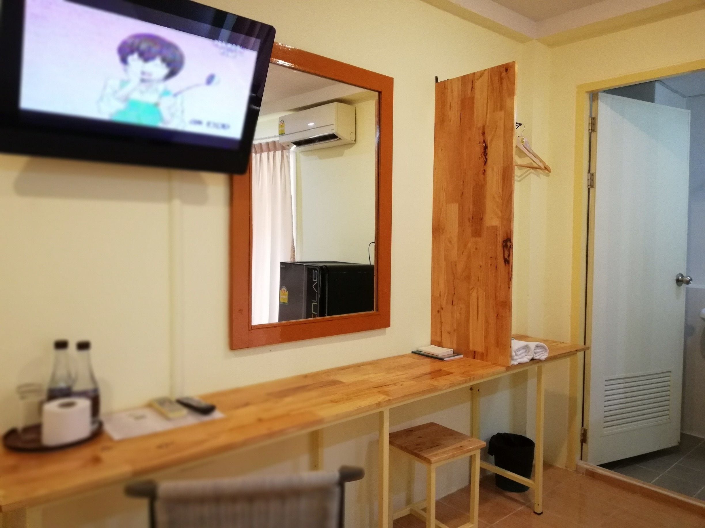 A room with a wooden desk, a mirror, a TV, a heater, and a door.