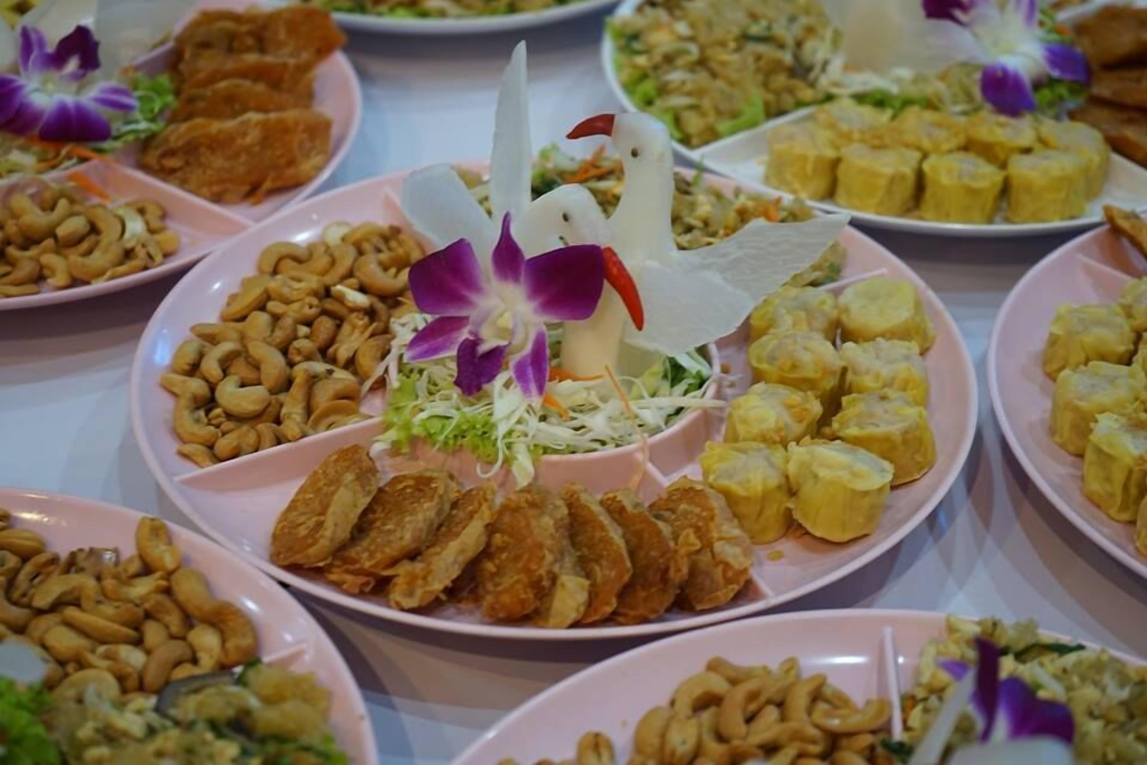 Una mesa con diversos platos, incluyendo alimentos fritos, nueces de cajú y un centro de mesa decorativo con flores.