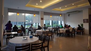 Un vaste espace dédié à la salle à manger, avec des tables et des chaises rondes, de grandes fenêtres offrant une vue sur l’extérieur et un éclairage encastré au plafond.