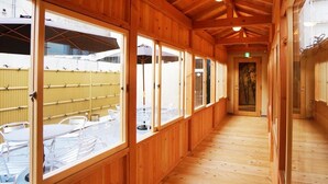 A corridor with wooden walls and large windows, leading to an outdoor seating area with tables and chairs.