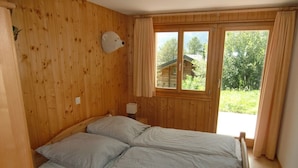 A wooden-paneled room with a bed, a headboard, a window, and a view of greenery outside. - 5 star chalet with stunning views, top location, free Wi-Fi, ski-in-ski-out (Bellwald)