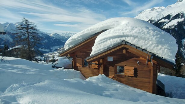 A wooden cabin with a snow-covered roof, surrounded by a snowy landscape and mountains. - 5 star chalet with stunning views, top location, free Wi-Fi, ski-in-ski-out (Bellwald)