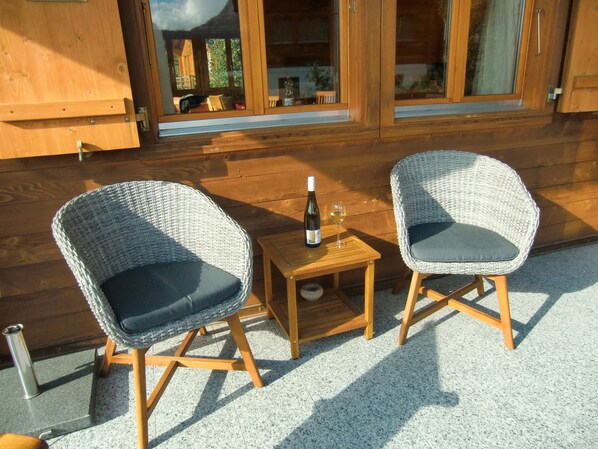 Two wicker chairs with cushions, a small wooden table, a bottle of wine, and a glass on the table. - 5 star chalet with stunning views, top location, free Wi-Fi, ski-in-ski-out (Bellwald)